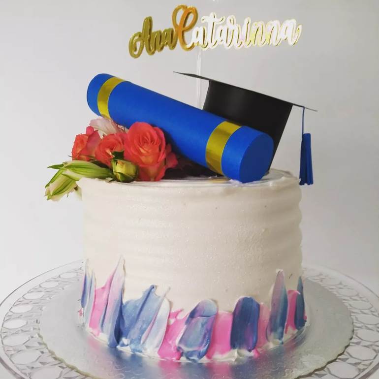 Bolo branco com detalhes rosa e lilás e diploma azul